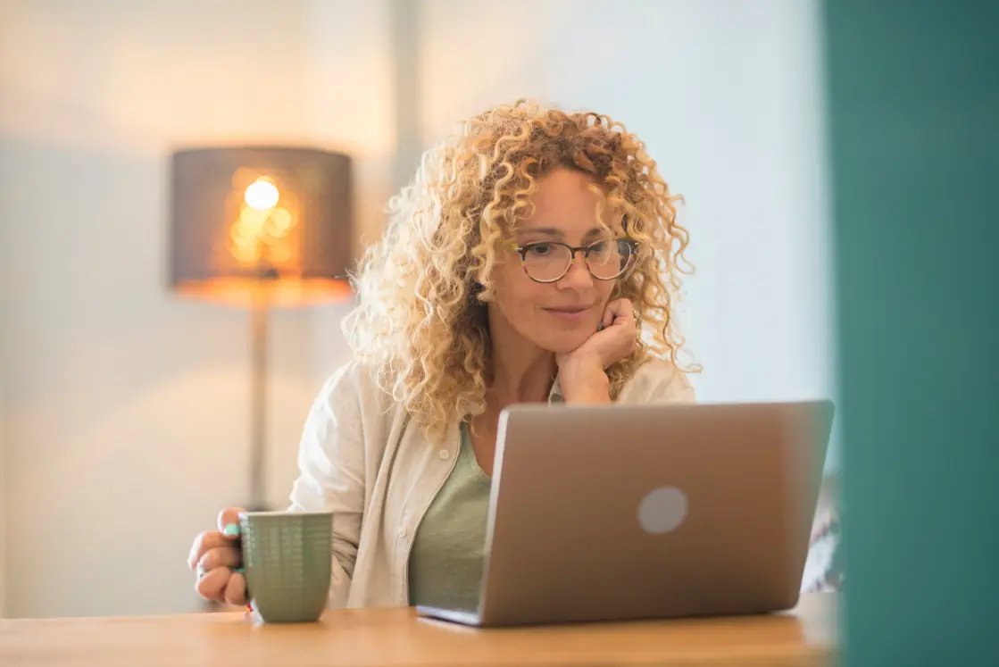 Lady sat at a table with a coffee and her laptop during an online therapy session