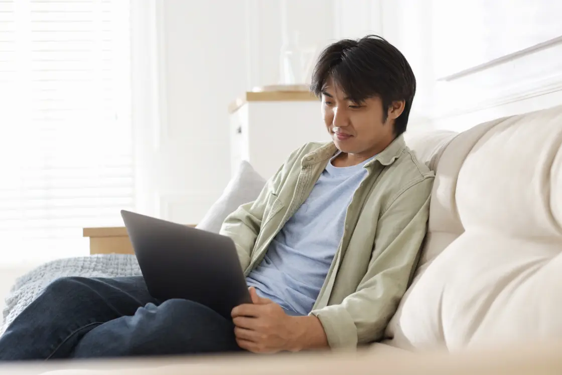 Man sat on the sofa looking down at his laptop during an online therapy session