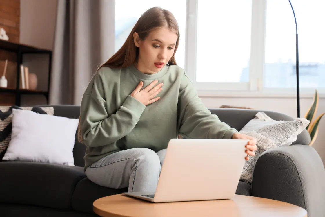 Lady sat on a sofa looking down at her laptop in conversation during her online therapy session