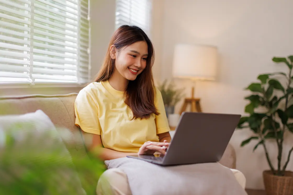 Lady sat on the sofa with her laptop on her lap, taking part in an online therapy session